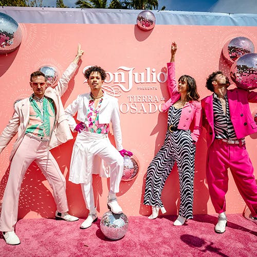 Four people in front of a pink backdrop at a Don Julio Rosado event