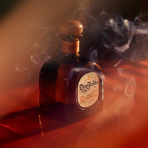 A bottle of Don Julio Reposado with smoke floating in front of it on a brown and red background