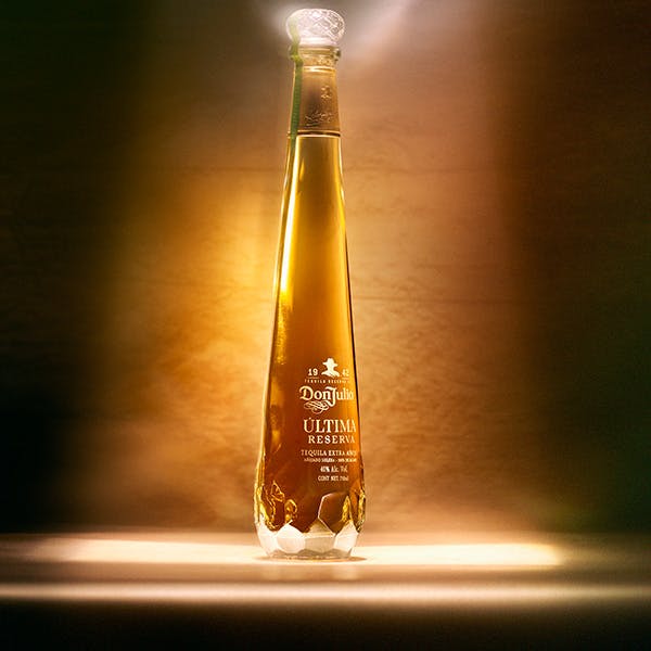 A bottle of Don Julio Ultima Reserve on a table in a dark room with a beam of light illuminating the bottle from above